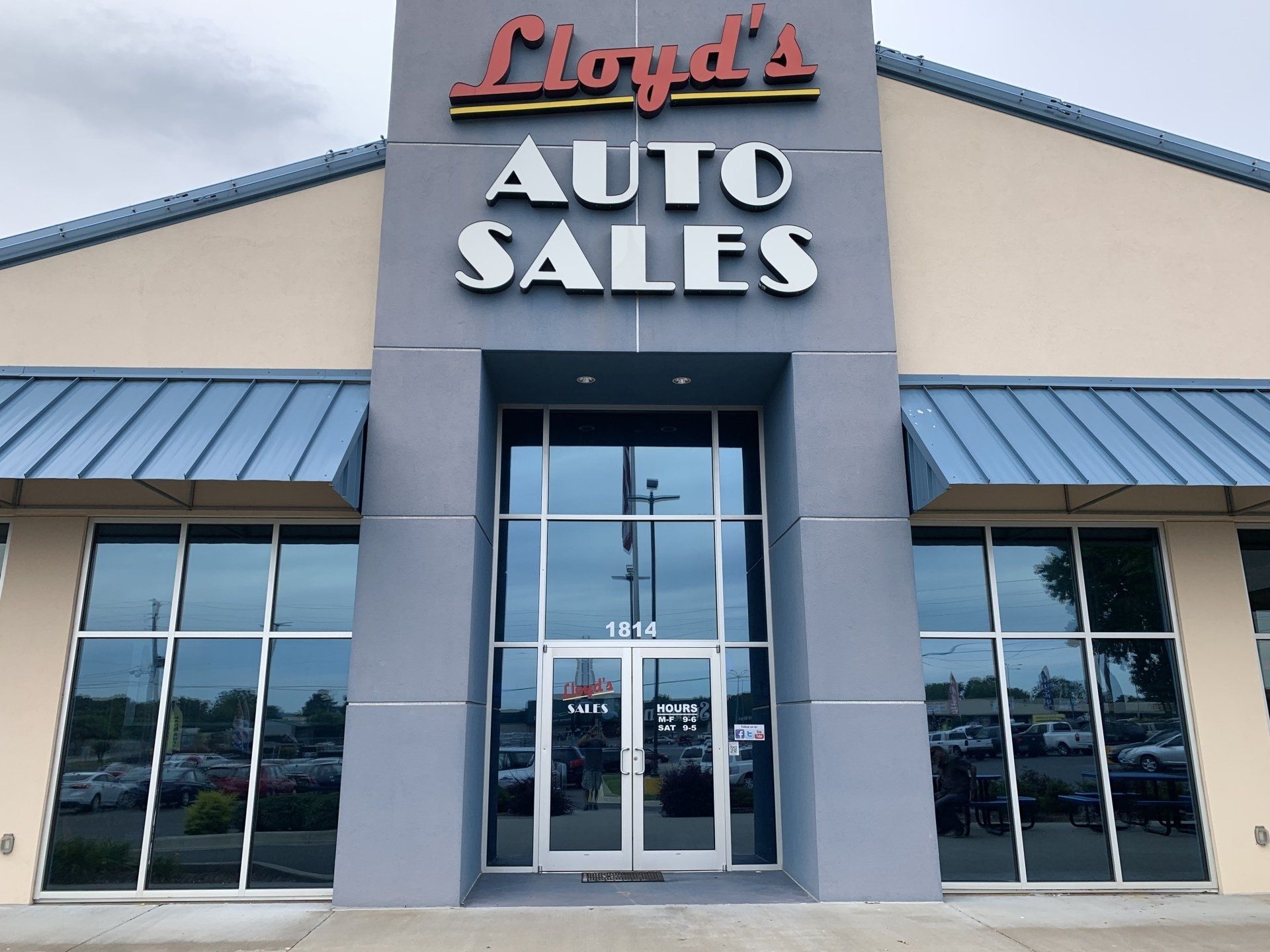 Lloyd's Auto Sales building with large windows and signage against a cloudy sky.