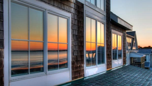 Windows reflecting a colorful sunset over a calm body of water; shingled building exterior.
