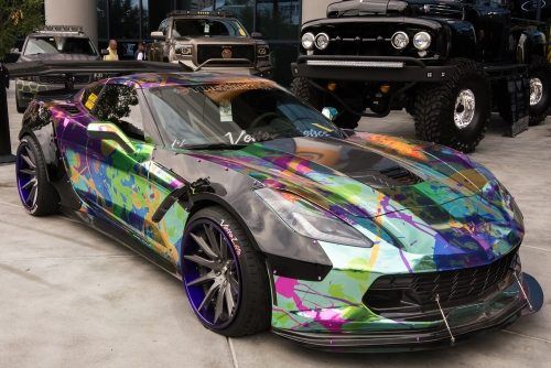 Customized Corvette with colorful paint, large wheels, and a rear spoiler, parked outdoors.