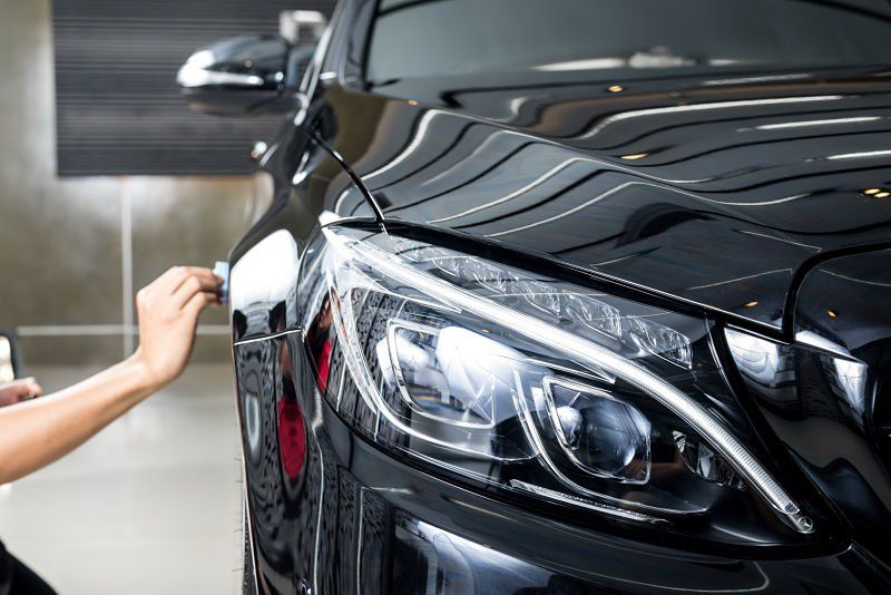 Hand polishing a shiny black car headlight in a professional setting.