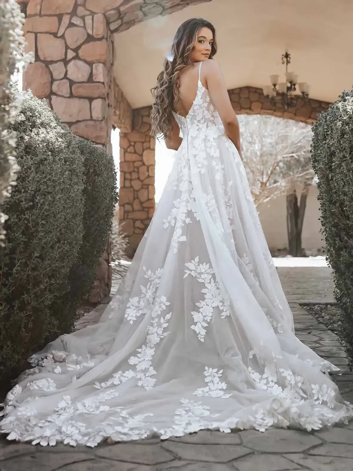 A woman in a white wedding dress is standing in front of a stone building.