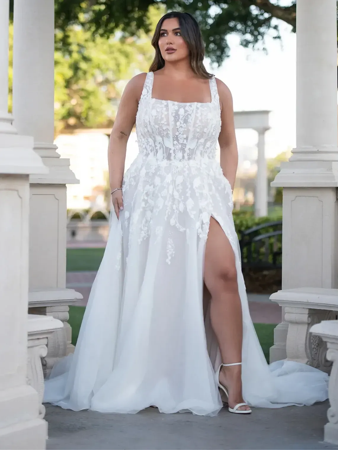 A plus size model is wearing a white wedding dress with a high slit.