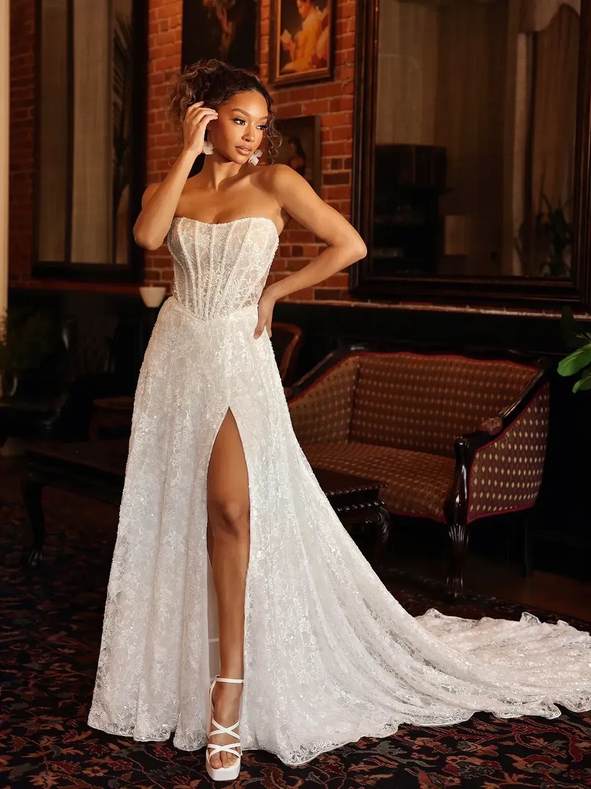 A woman in a white wedding dress with a high slit is talking on a cell phone.