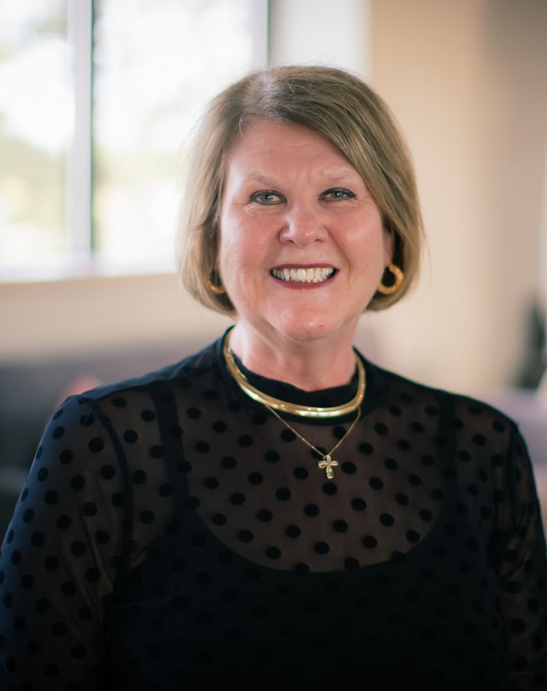 A woman wearing a black polka dot shirt and a gold necklace is smiling for the camera.