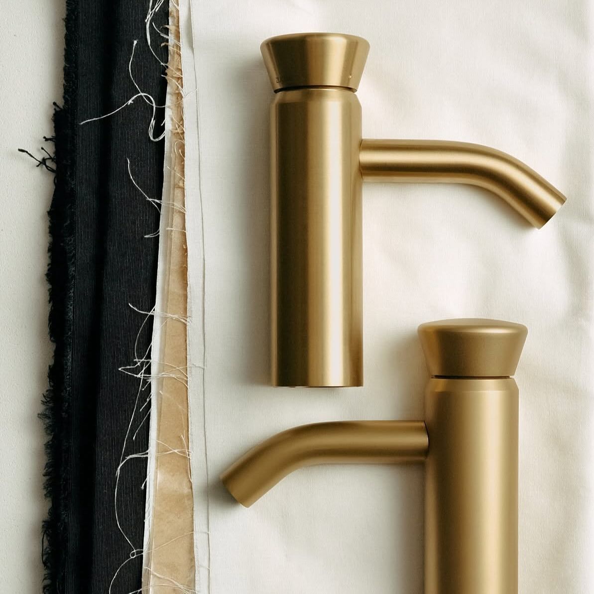 Due rubinetti color oro con beccucci curvi su una superficie testurizzata color bianco sporco.