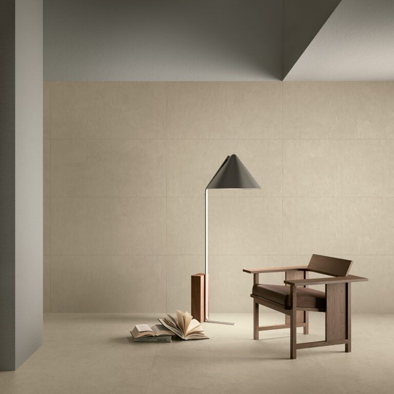 Interno minimalista: sedia, lampada, libri contro pareti e pavimento beige chiaro.