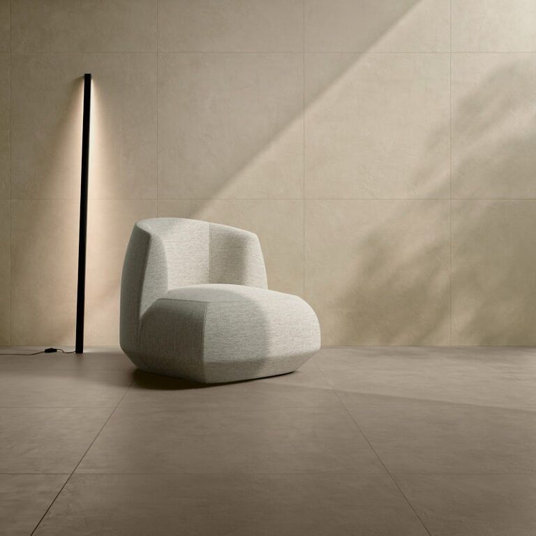 Moderna poltrona beige accanto a una lampada da terra nera contro una parete beige chiaro.