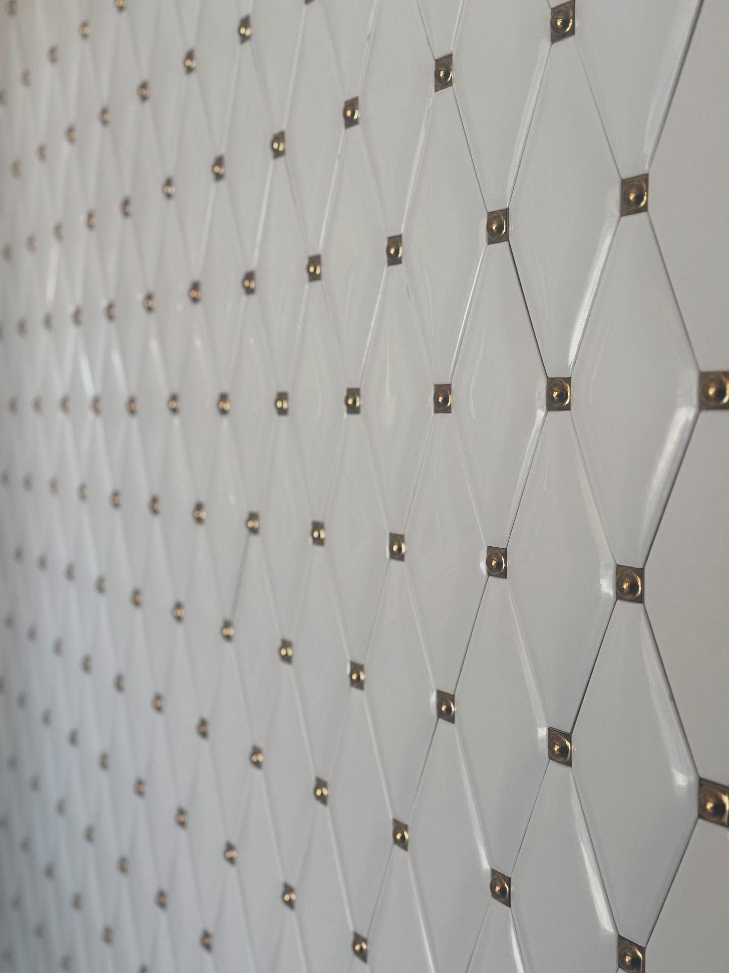 Parete bianca con motivo a rombi, impreziosita da borchie dorate.