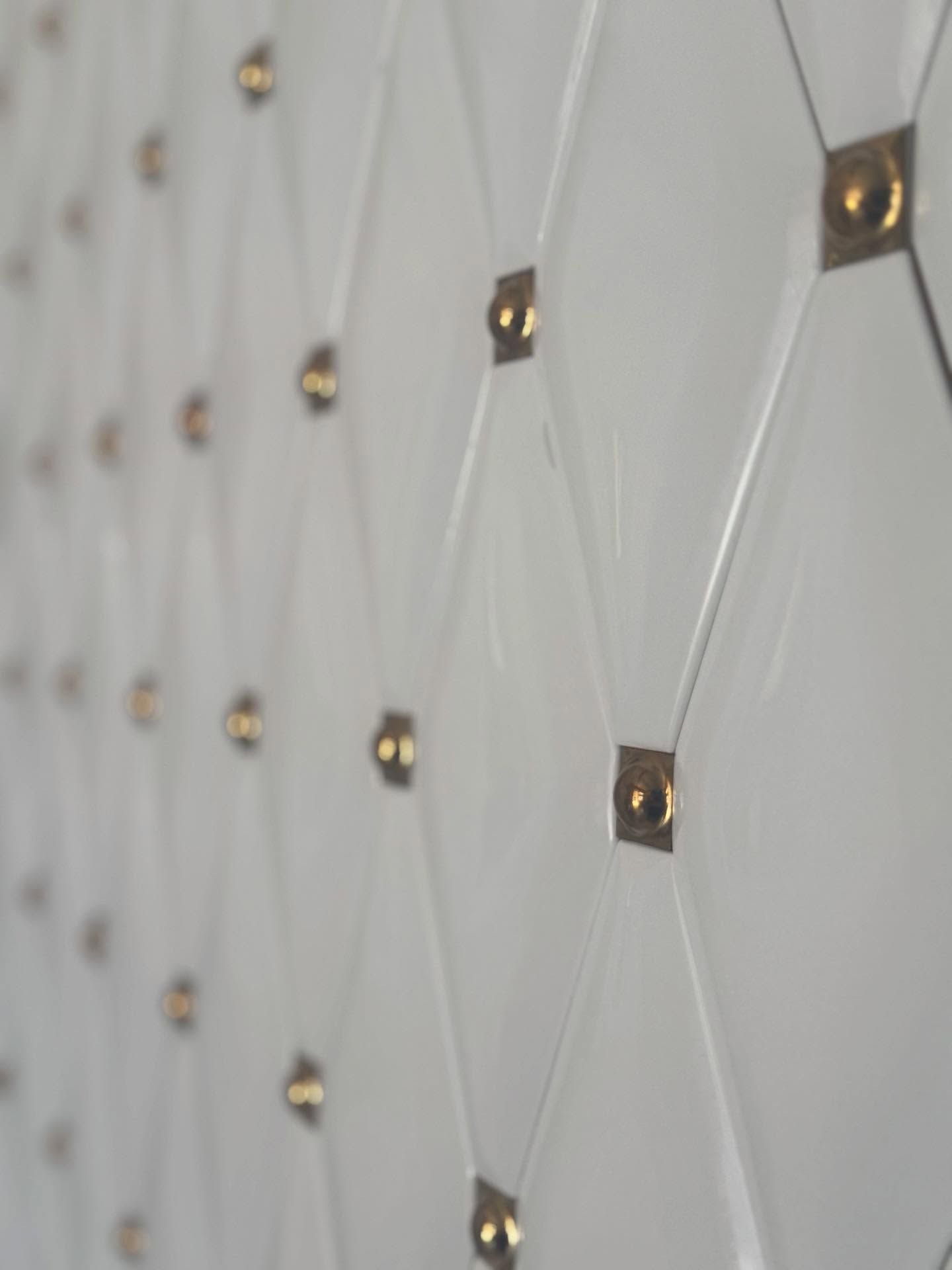 Parete bianca con motivo a rombi, impreziosita da borchie dorate.