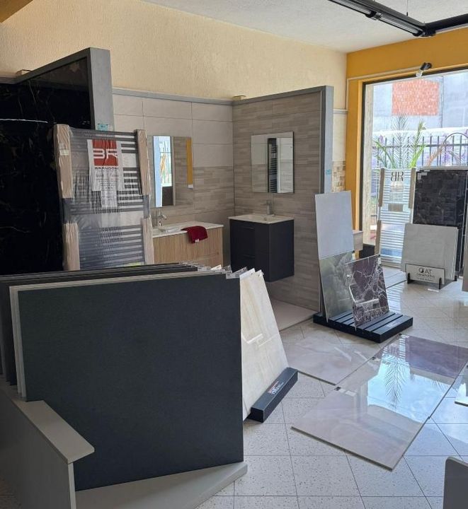 Interno dello showroom di piastrelle con bagno in esposizione e campioni di pietra impilati.