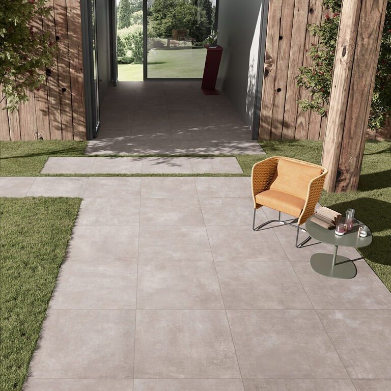 Patio con piastrelle in pietra, sedia, tavolino e porta aperta su un cortile con alberi ed erba.