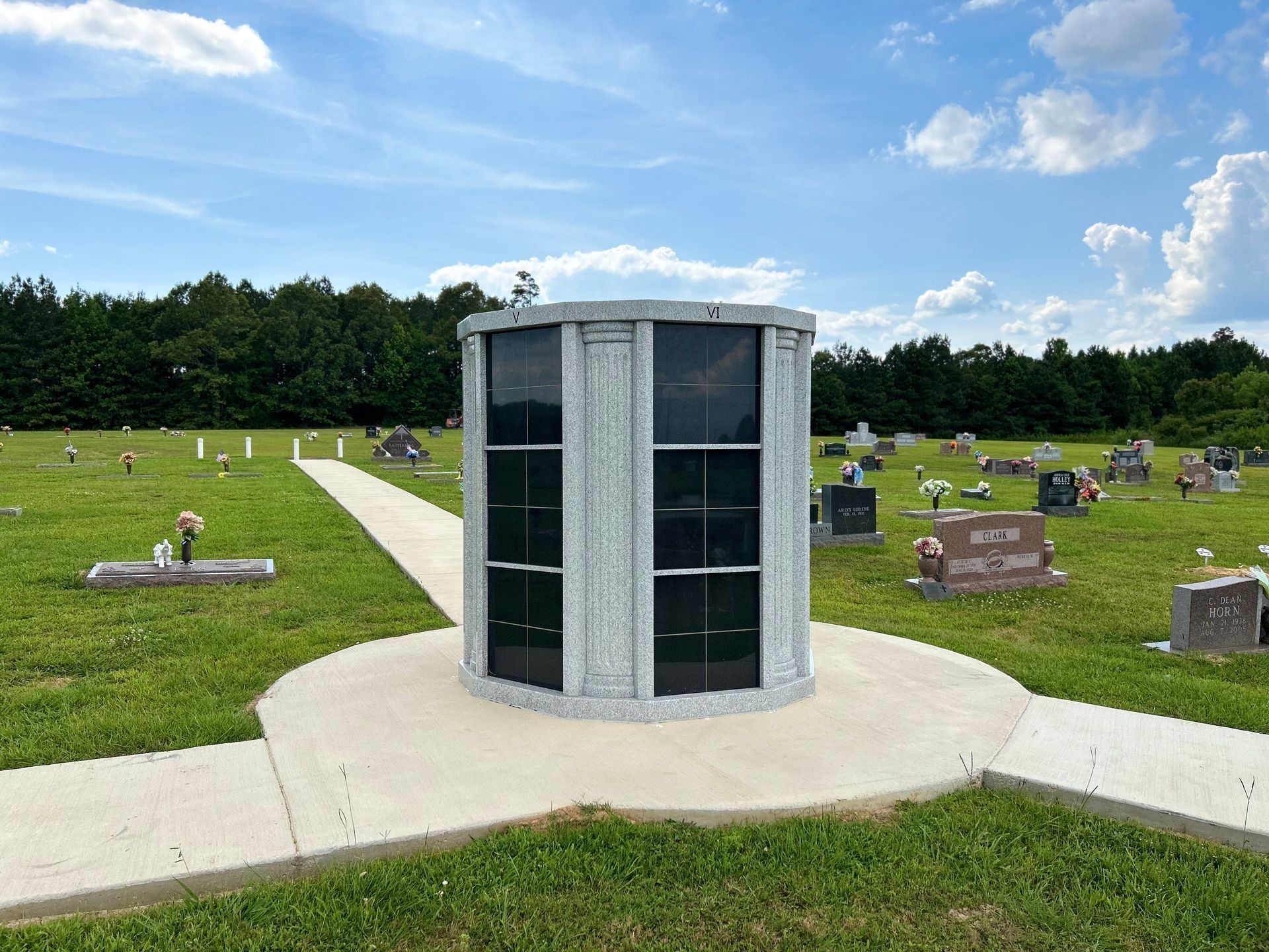 Cylindrical columbarium in a cemetery with green lawns, headstones, and a blue sky