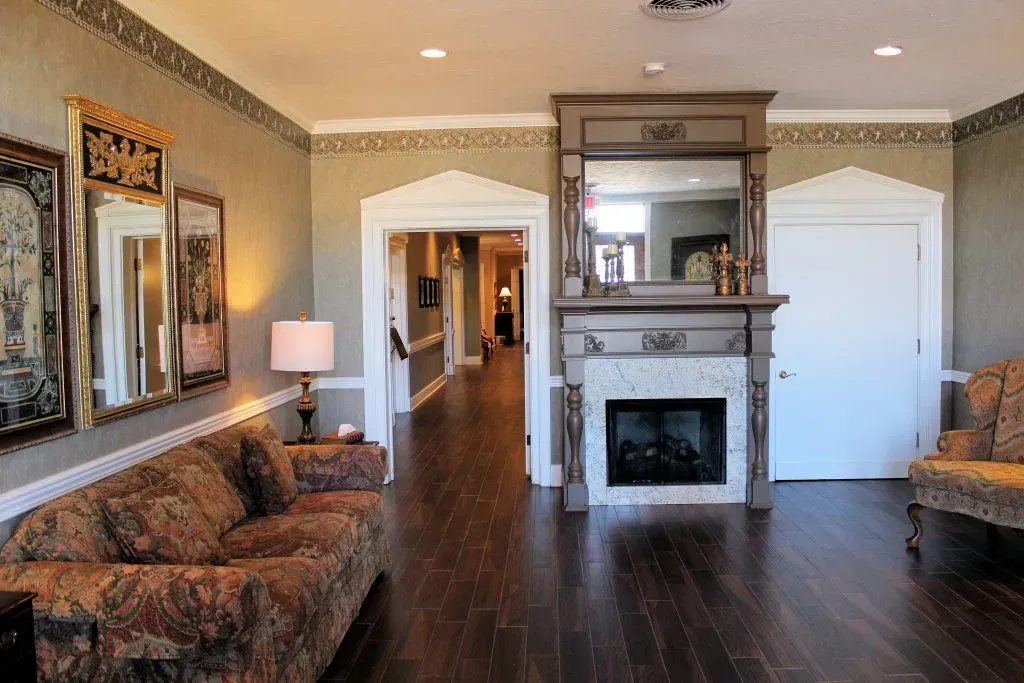 Living room with dark wood floors, fireplace, sofas, lamp, and hallway in the background