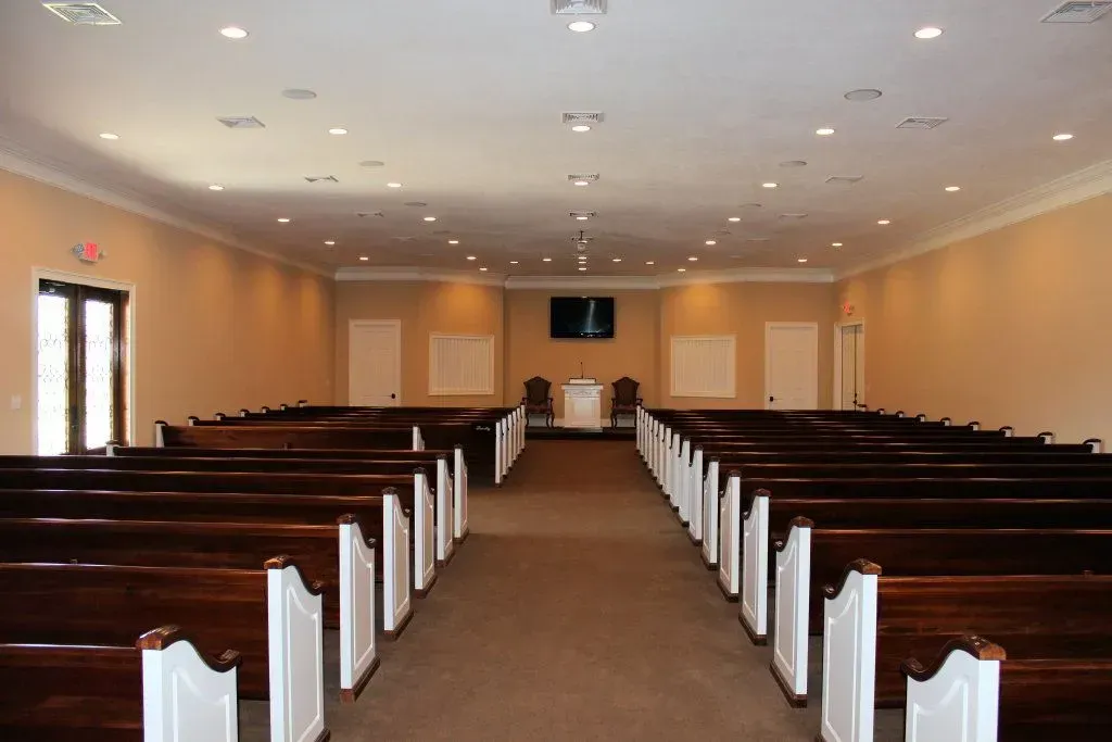 Empty church sanctuary with rows of wooden pews, white walls, and a central aisle facing the altar.