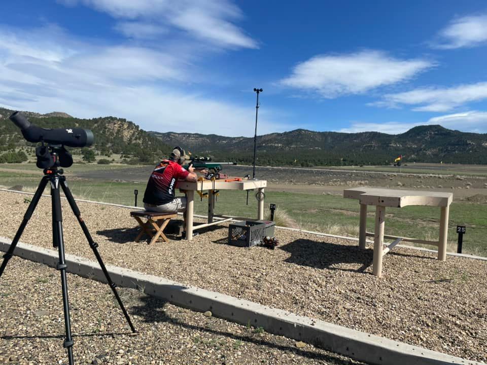 A man is sitting at a table in a field with a telescope on a tripod.