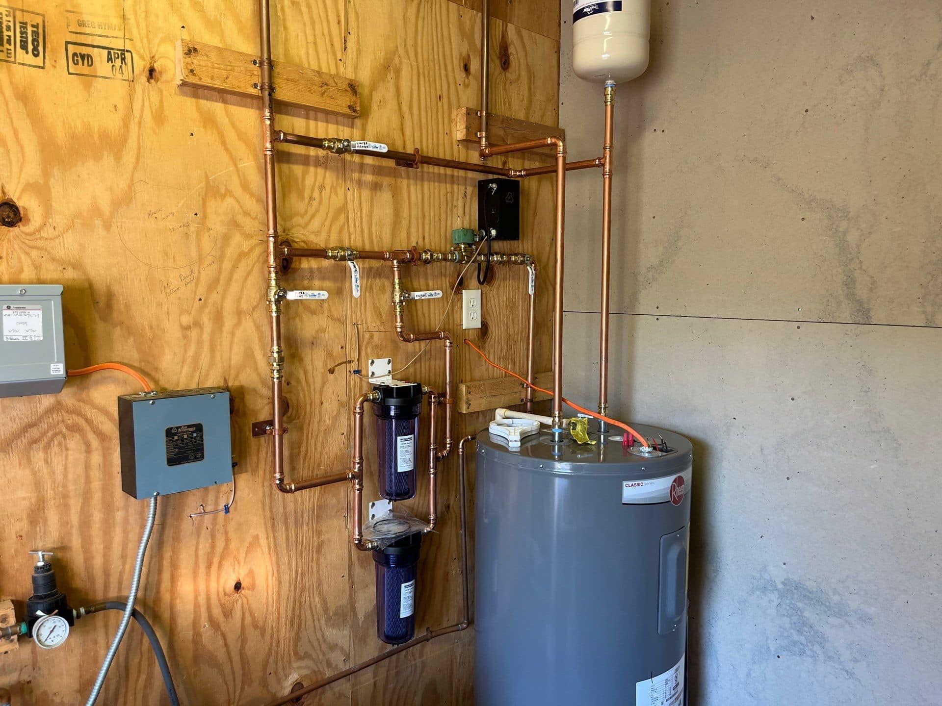 A room with a water heater and pipes on the wall.