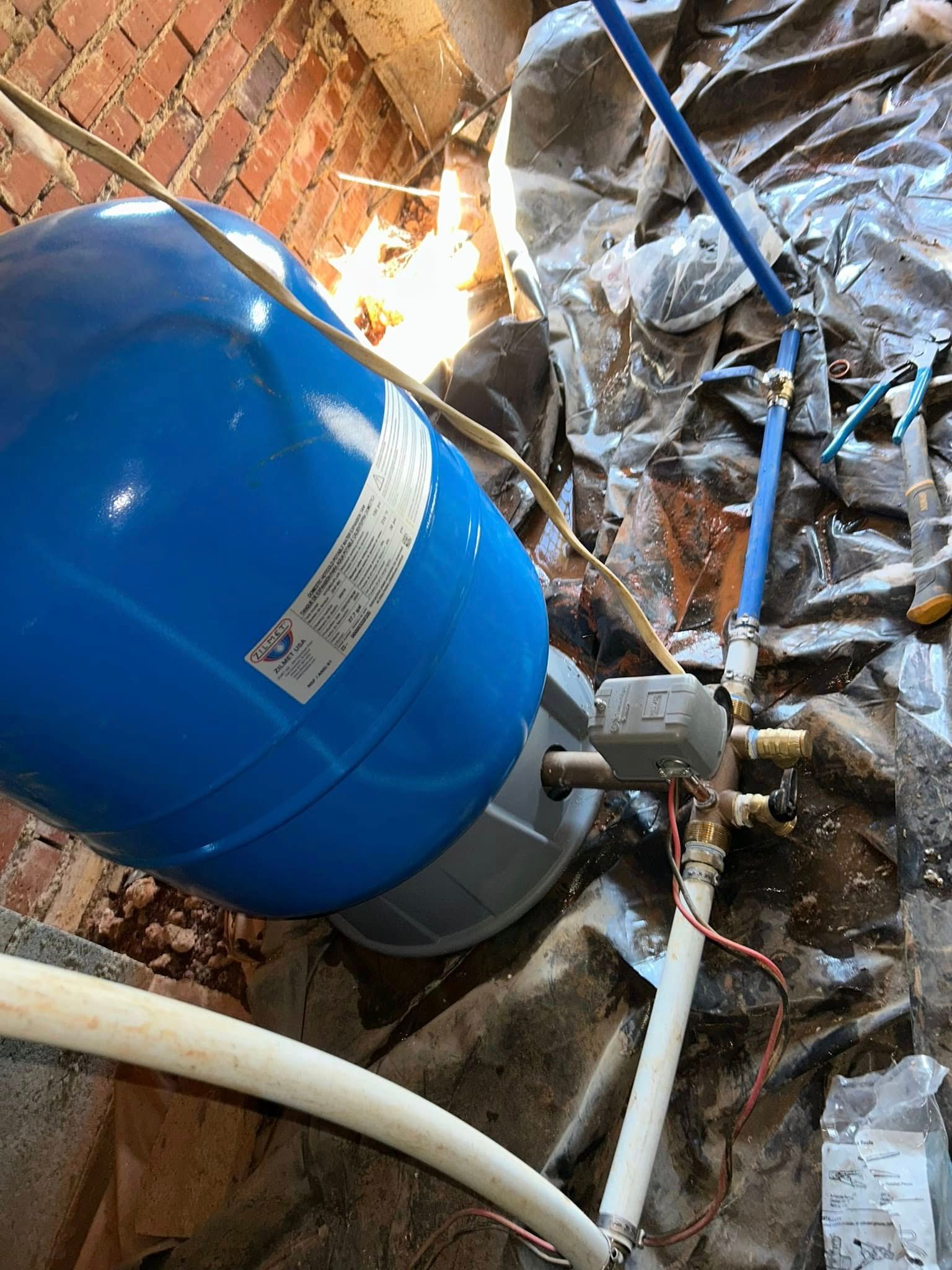 A blue water tank is sitting on the floor next to a brick wall.