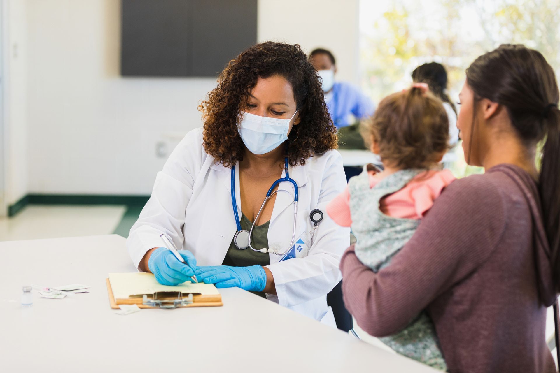 A doctor wearing a mask is talking to a woman holding a baby.
