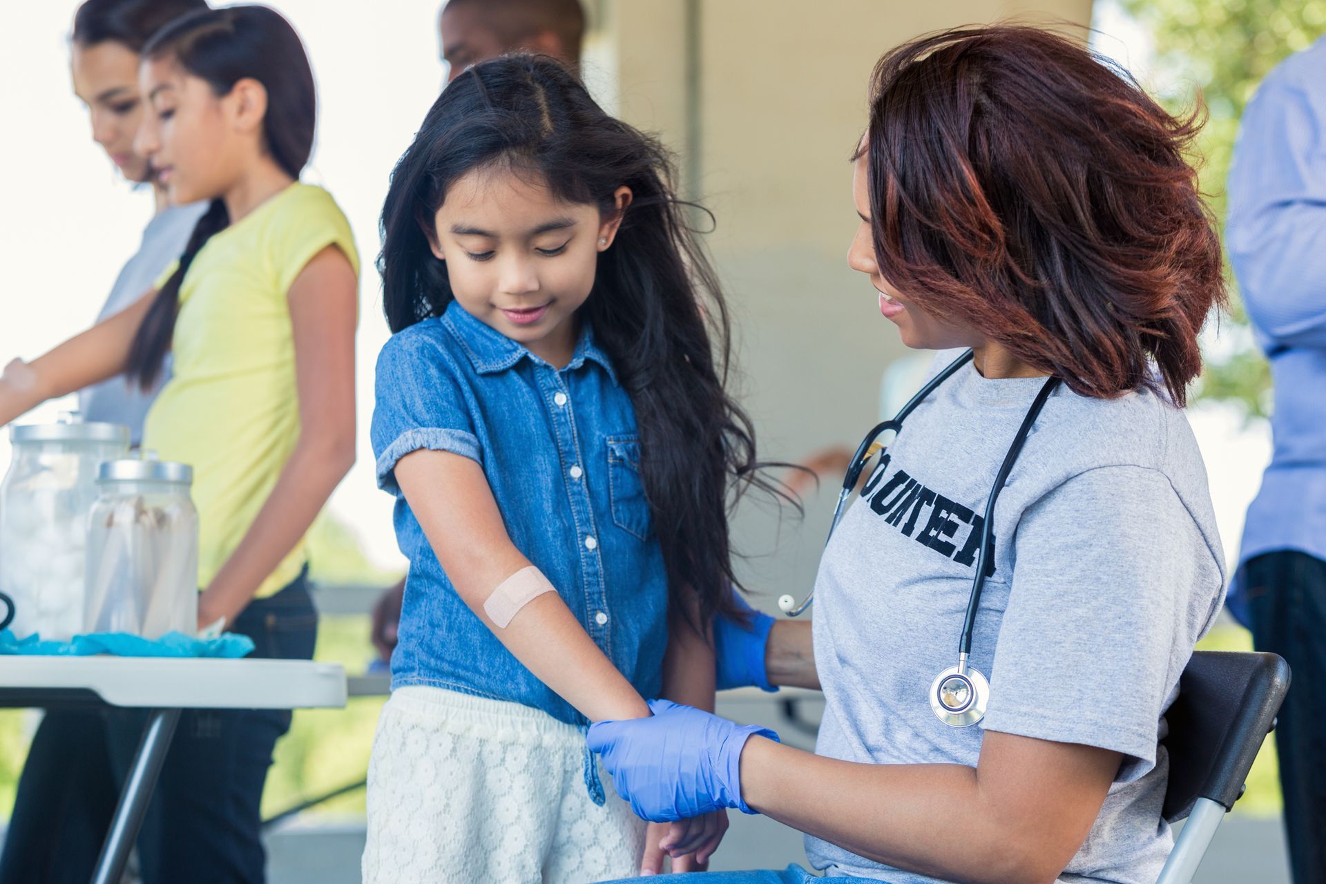 A woman is giving a girl a bandage on her arm.