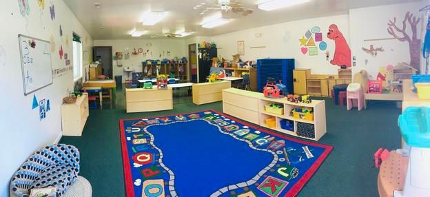 A large classroom with a blue rug and lots of toys.