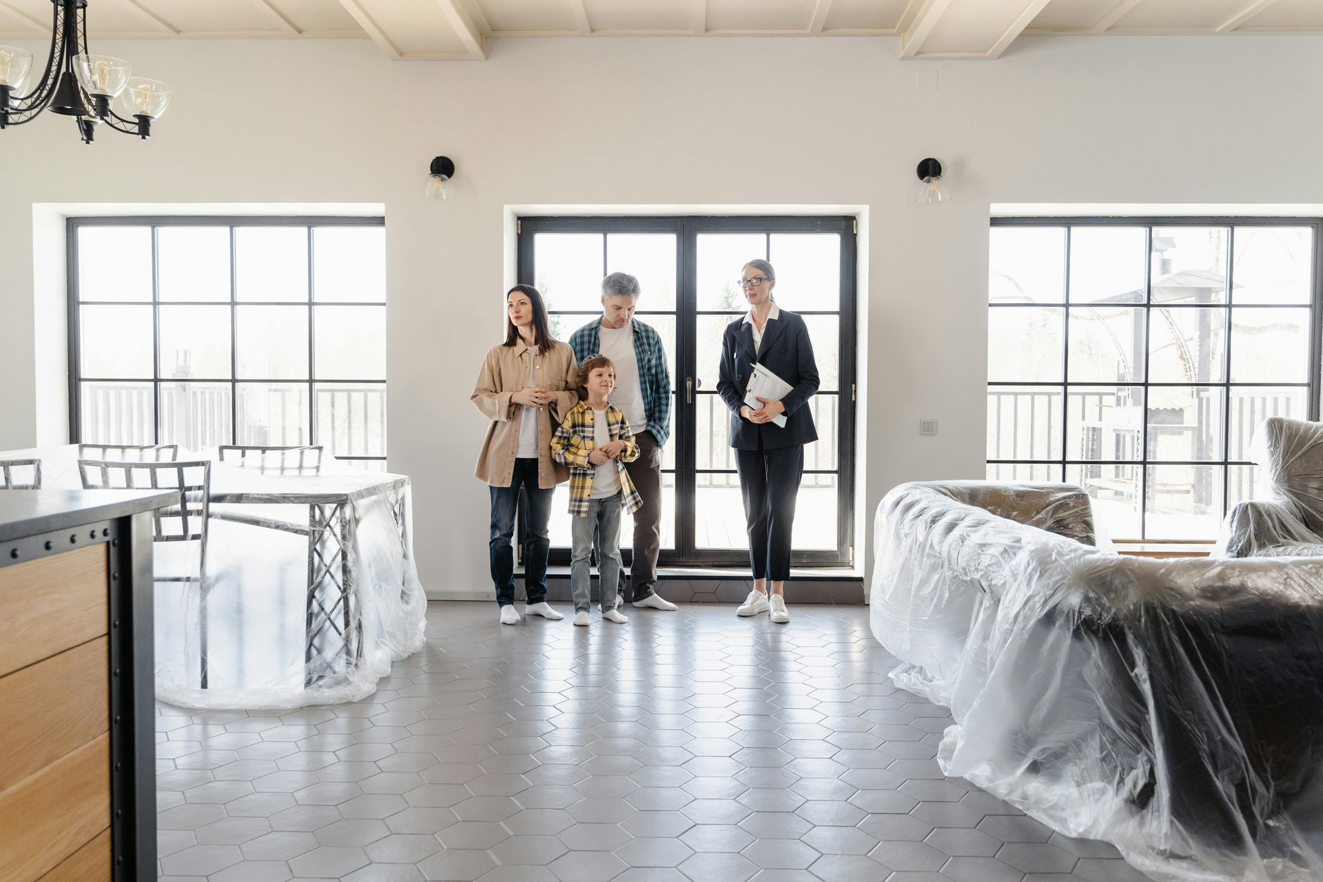 A family stands in a bright, modern living room under renovation, with furniture covered in plastic sheeting.