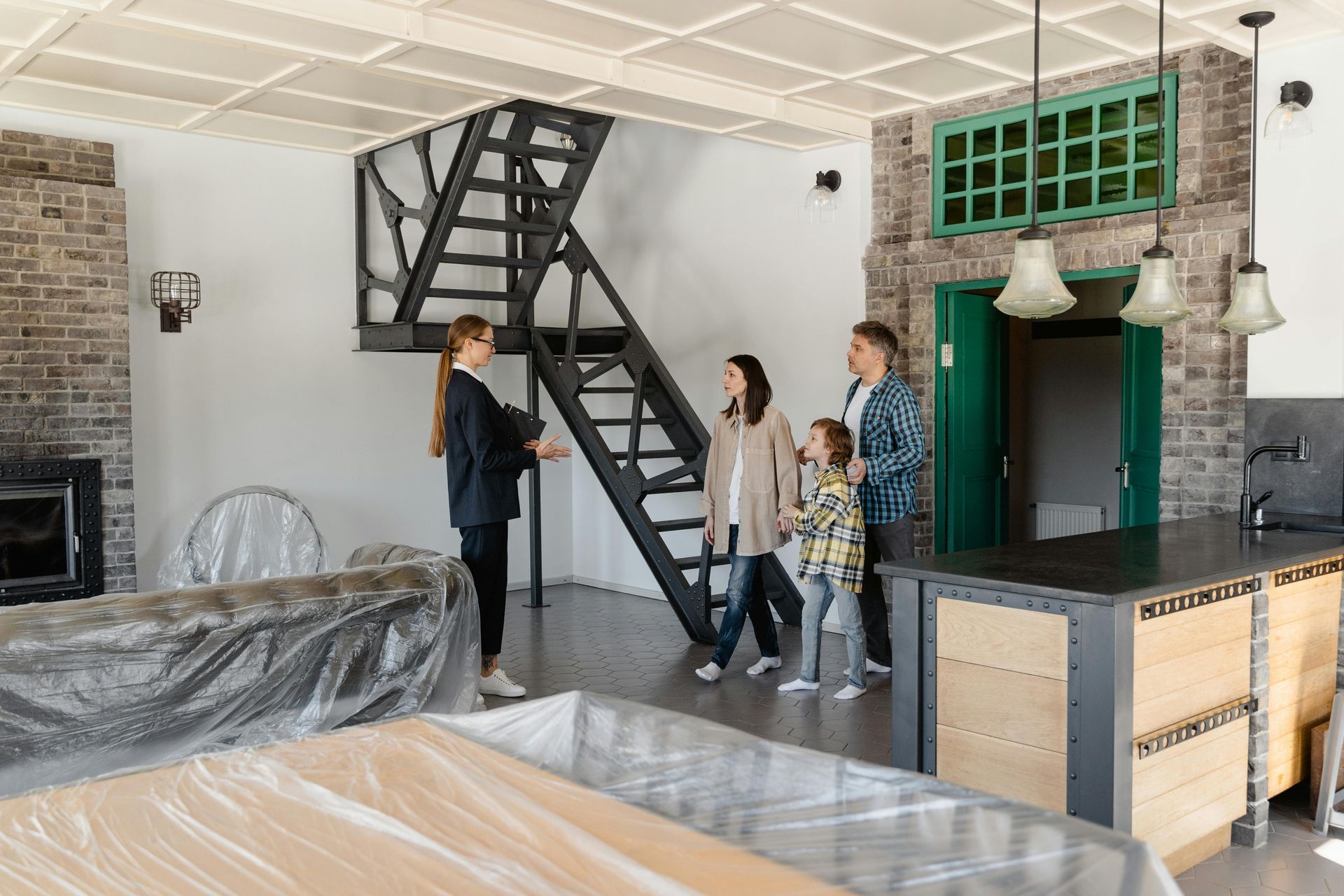 A real estate agent shows a family a modern, open-plan home featuring a metal staircase and brick walls.