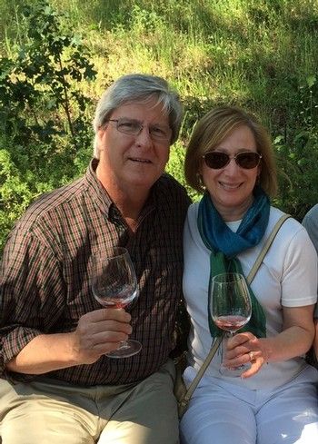 A man and woman sit outdoors, smiling and holding glasses of wine.