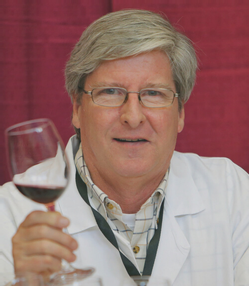 A person in a white coat holds up a glass of red wine against a red background.
