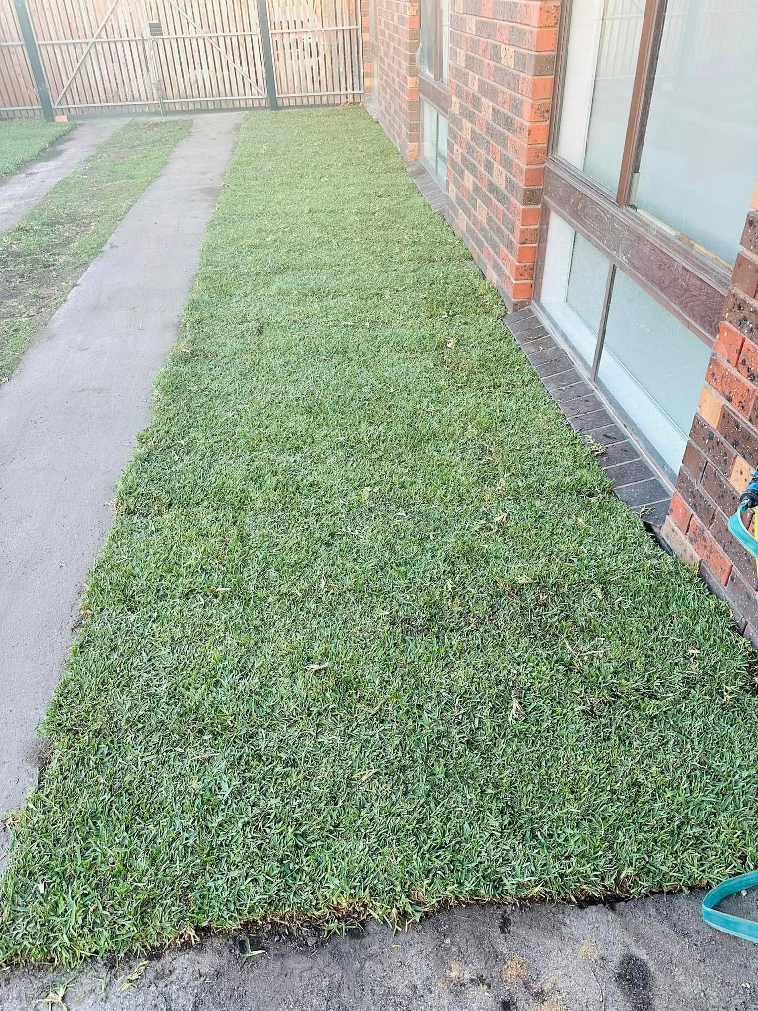 A lawn with a sidewalk and a brick building in the background.b