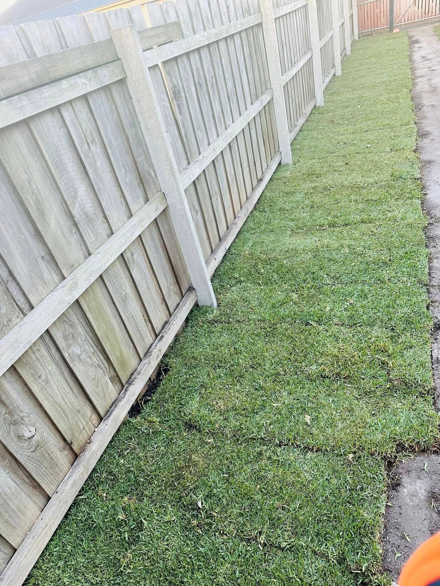 A person is standing next to a wooden fence and a pile of grass.