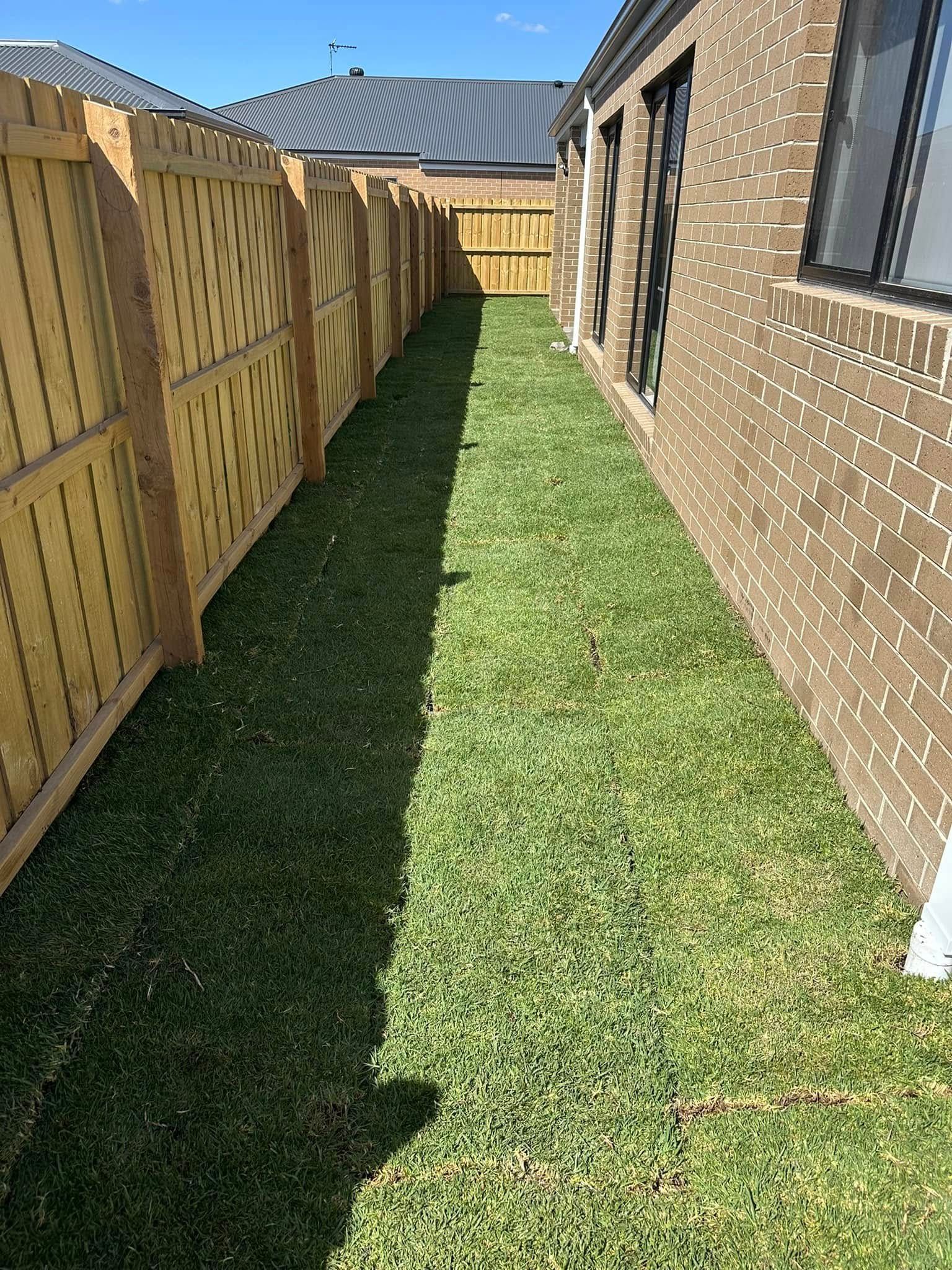A brick house with a wooden fence and a lush green lawn.