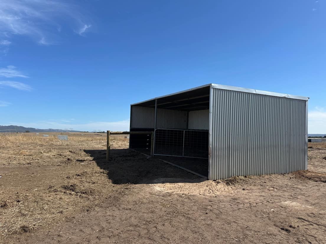 A metal shed is sitting in the middle of a dirt field.
