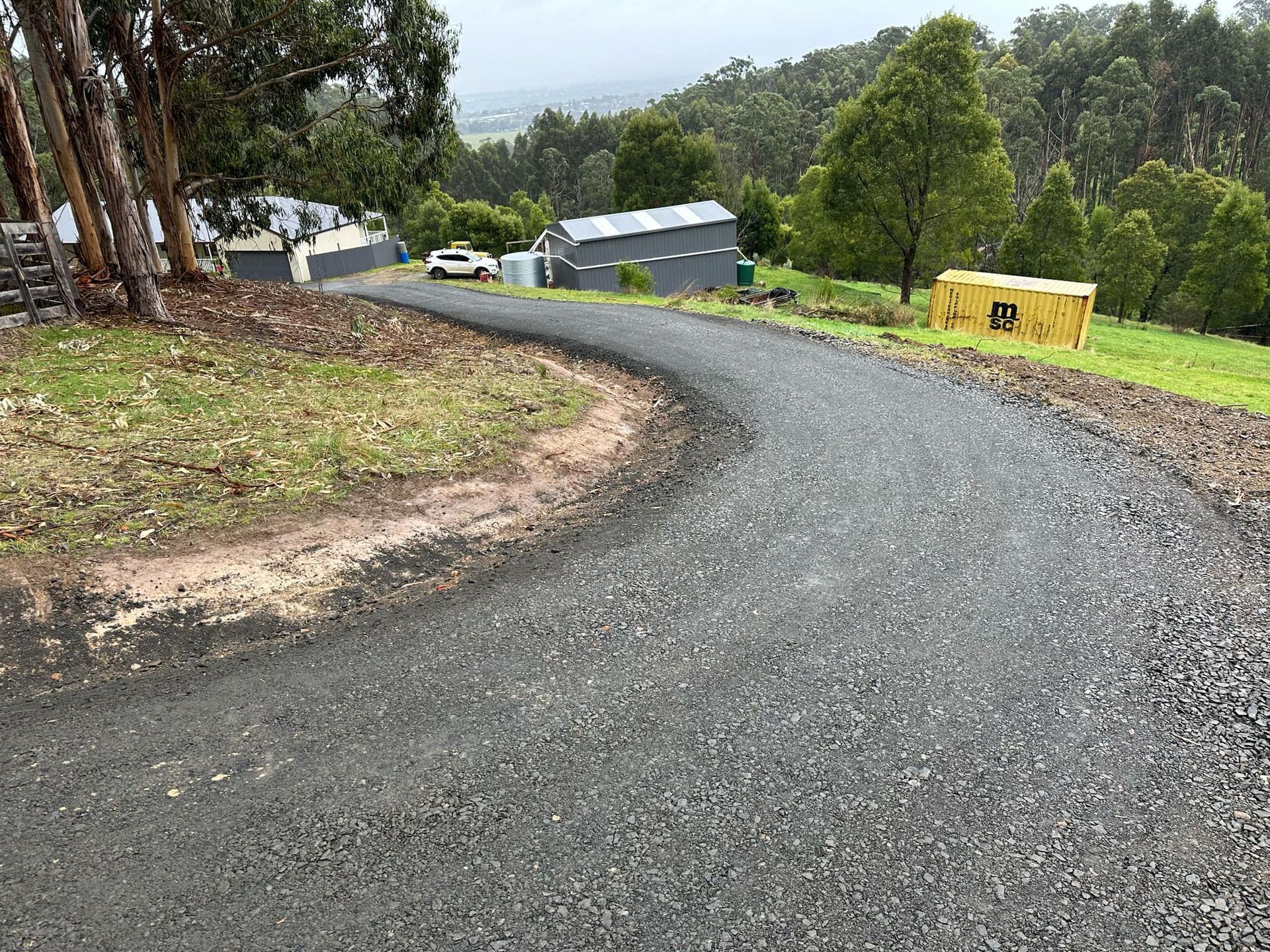 A curvy road going through a grassy hillside with trees on both sides.