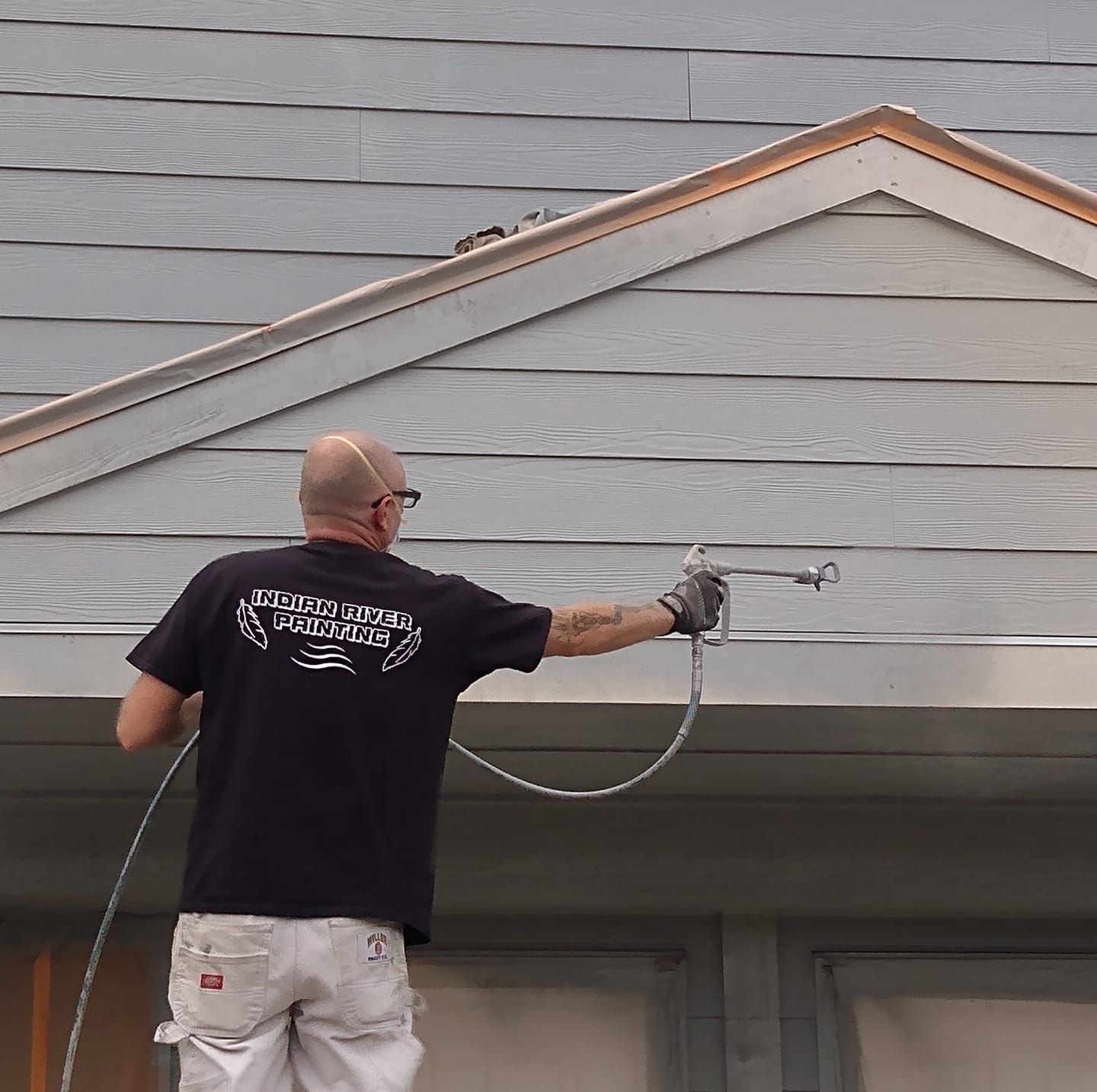A man is spray painting the side of a house