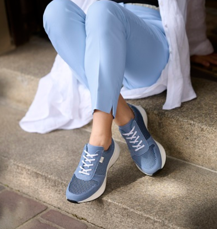 A woman wearing blue pants and blue sneakers sits on a set of steps