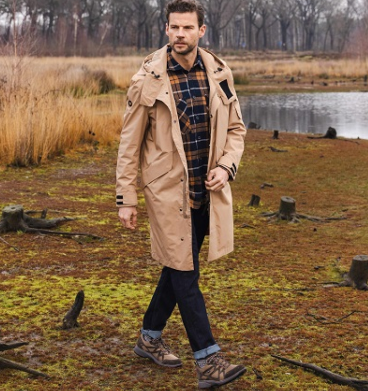 A man in a trench coat is walking in a field