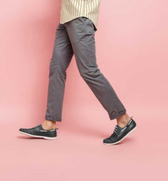 A person wearing gray pants and black shoes is walking on a pink background