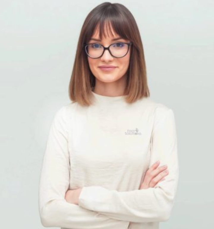 A woman wearing glasses and a white sweater is standing with her arms crossed.