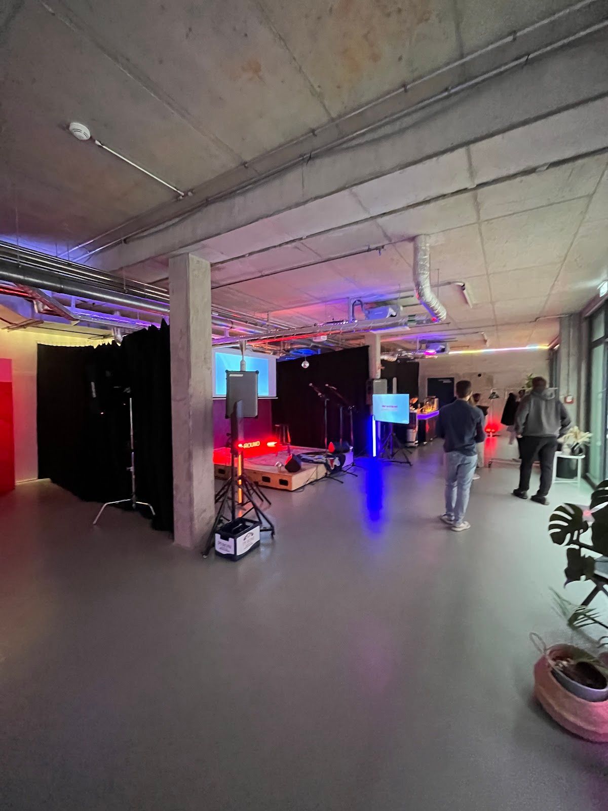 Ein Veranstaltungsraum im Innenbereich mit kleiner Bühne, Licht- und Tontechnik. Menschen stehen im Raum.