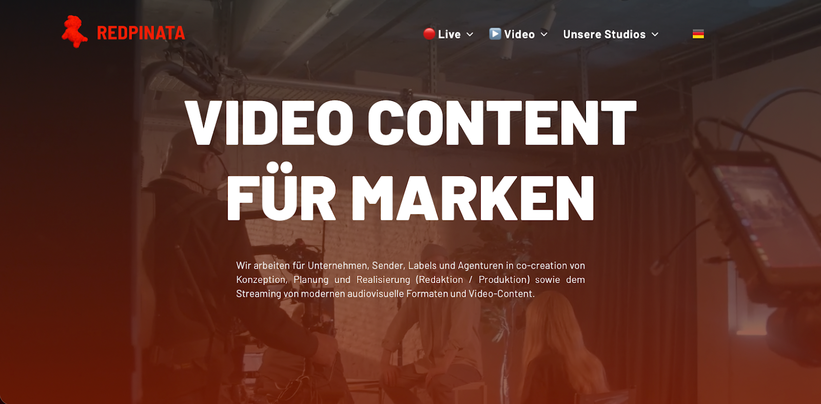 Header einer professionellen Videoproduktions-Website mit dem Text „VIDEO CONTENT FÜR MARKEN“ vor einem verschwommenen Filmset-Hintergrund.