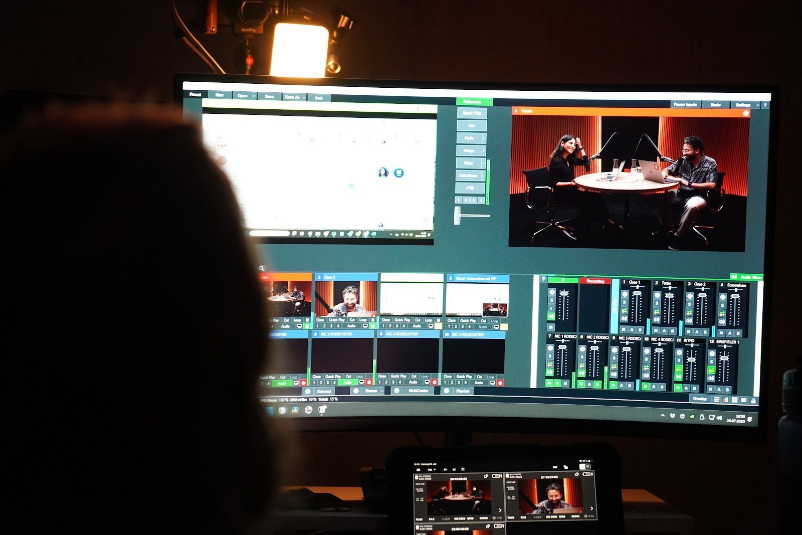 Eine Person überwacht eine Live-Stream-Produktion auf einem Computerbildschirm, auf dem mehrere Kameraperspektiven und Bearbeitungssoftware angezeigt werden.