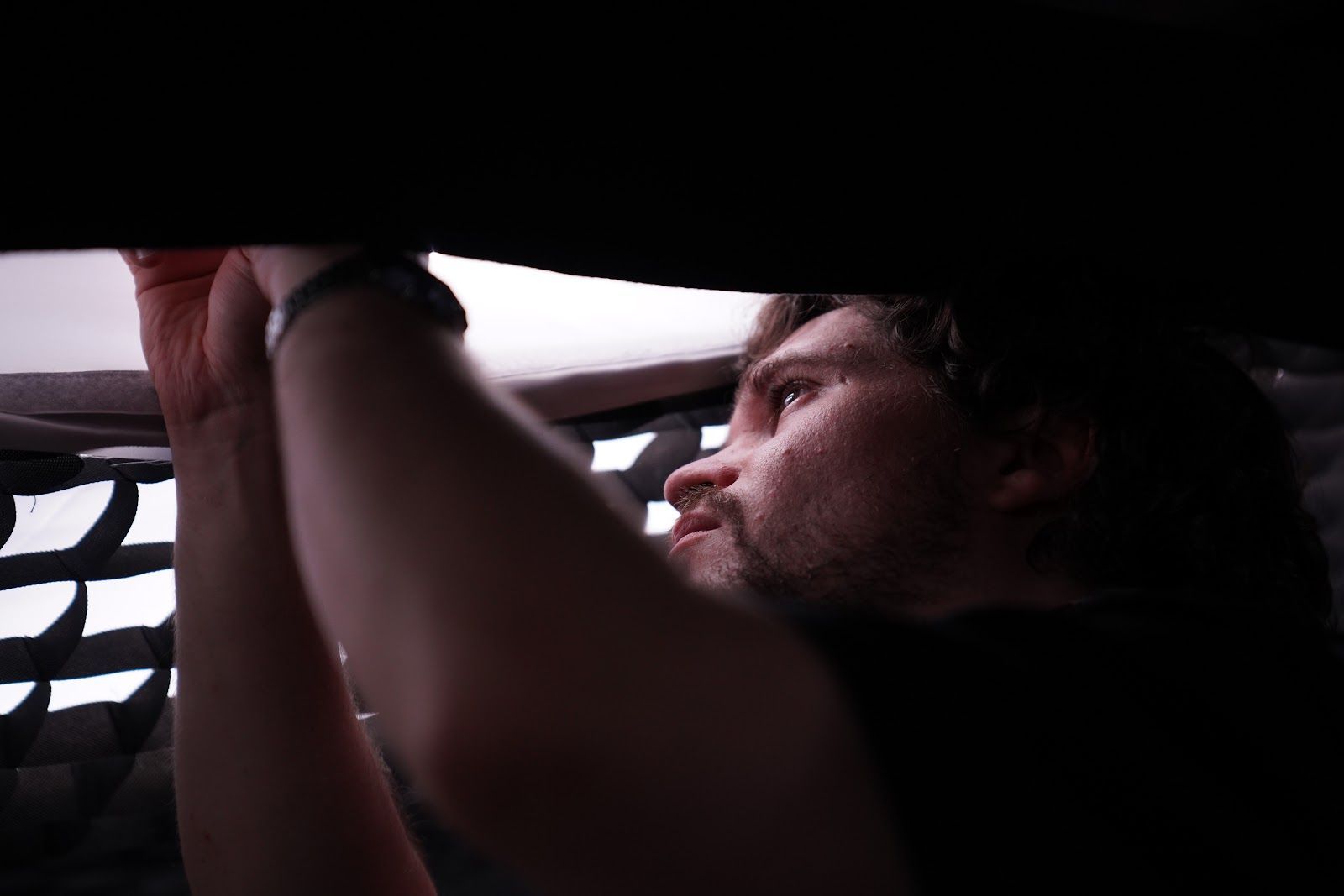 Eine Person mit hellbraunem Haar und Bart streckt die Hand aus, um ein weißes Stoffgebilde vor einem dunklen Hintergrund zurechtzurücken oder festzuhalten.