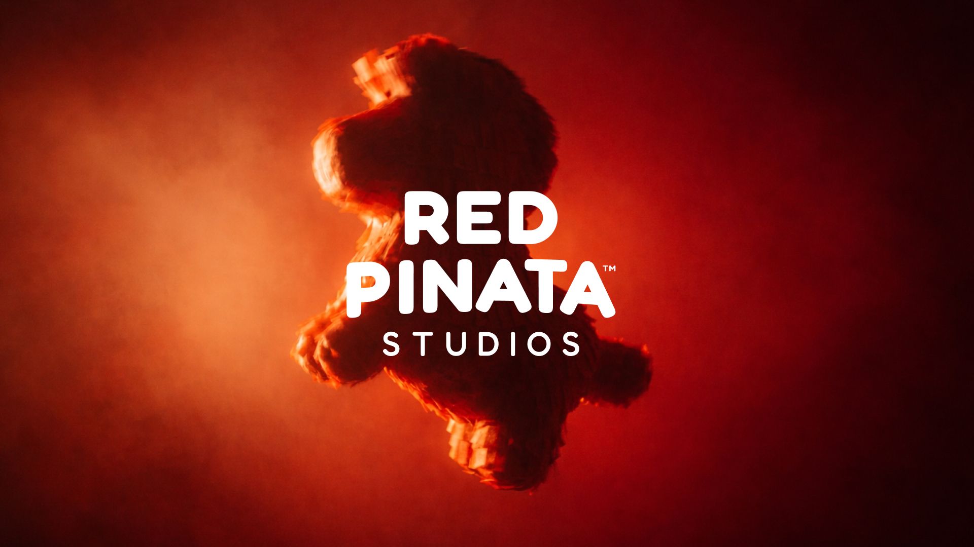 Vor einem roten, verschwommenen Hintergrund schwebt der weiße, blockartige Text „RED PINATA STUDIOS“ über einer verschwommenen, roten Piñata-Silhouette.