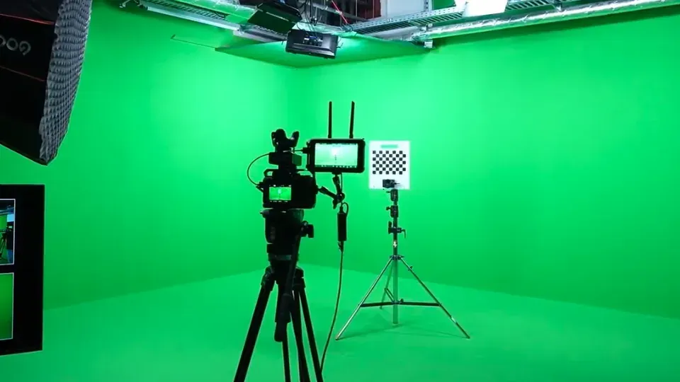 Eine auf einem Stativ montierte Videokamera ist in einem hellen Greenscreen-Studio auf ein schachbrettartiges Kalibrierungsziel gerichtet.