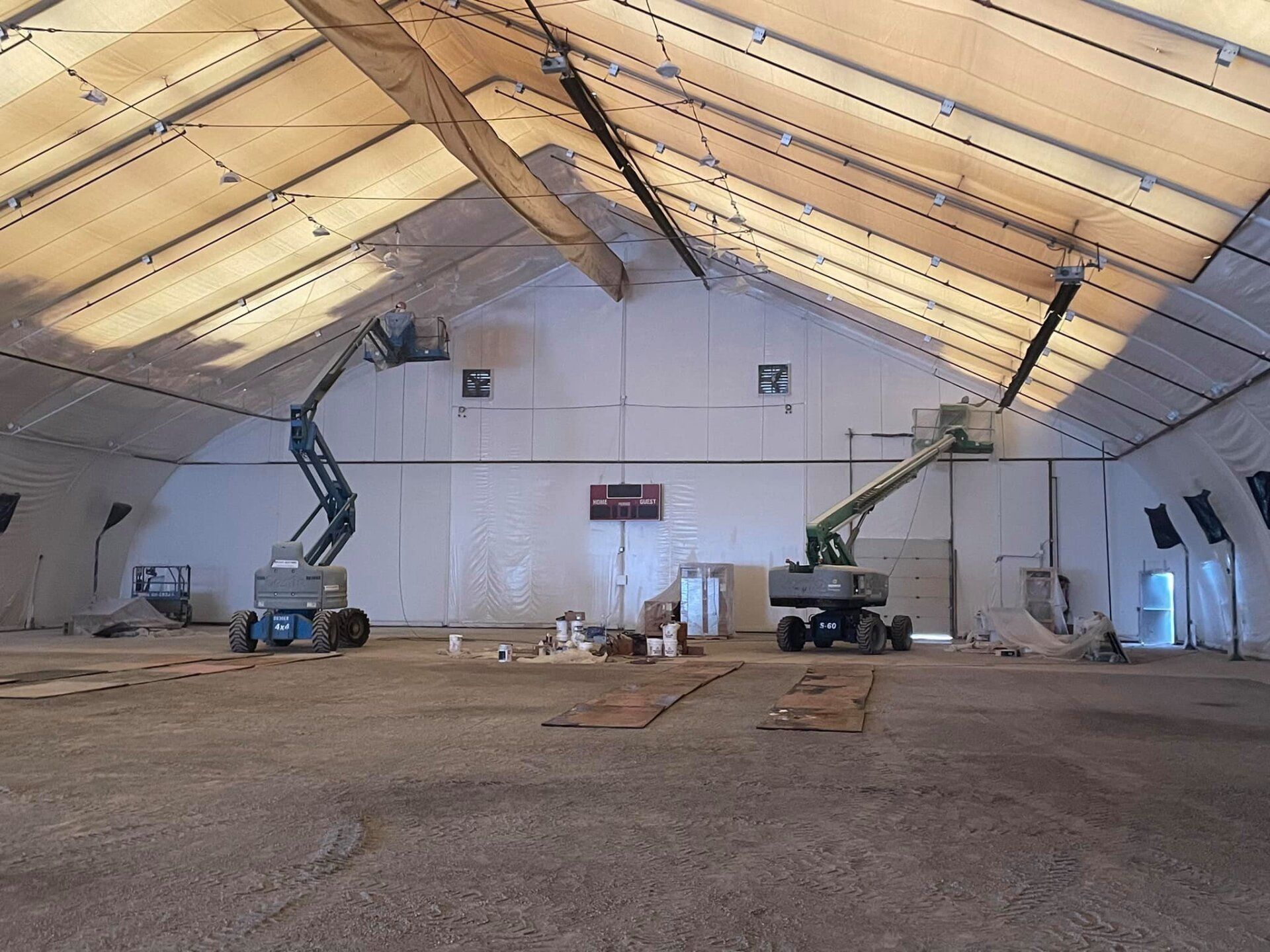 Interior painting of an indoor sports arena, with painters using boom lifts for high to reach areas in the stadium