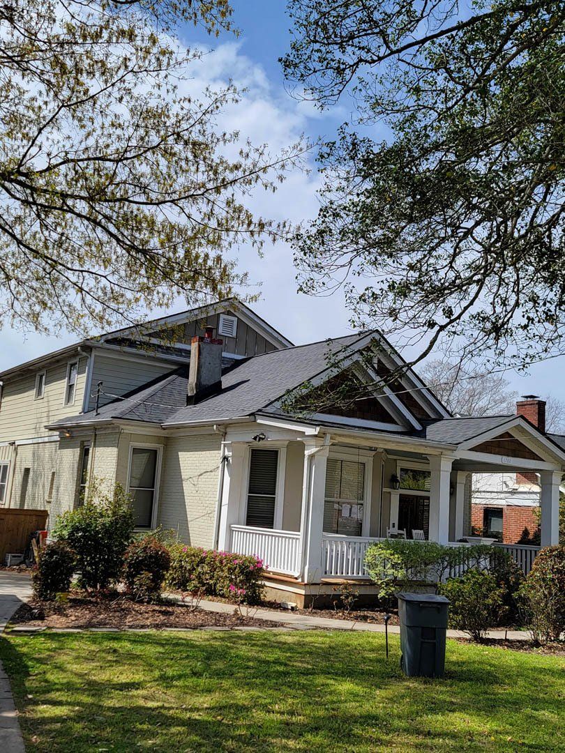 A white house with a porch and a trash can in front of it.