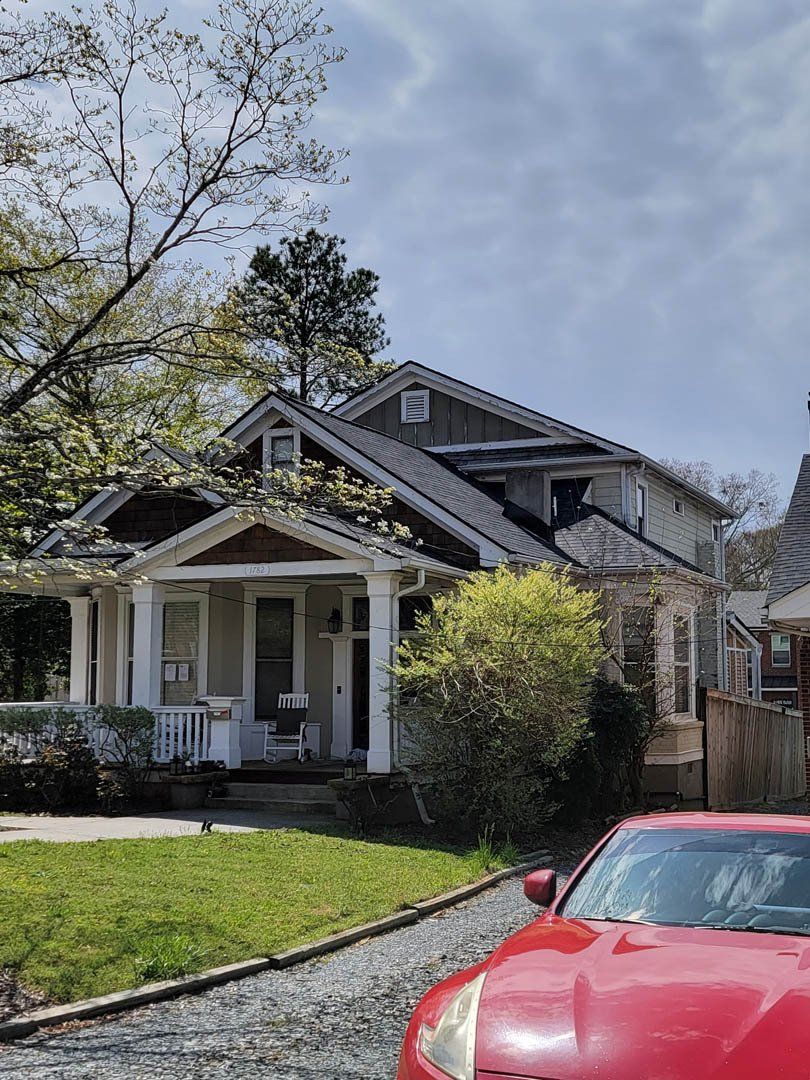 A red car is parked in front of a white house.