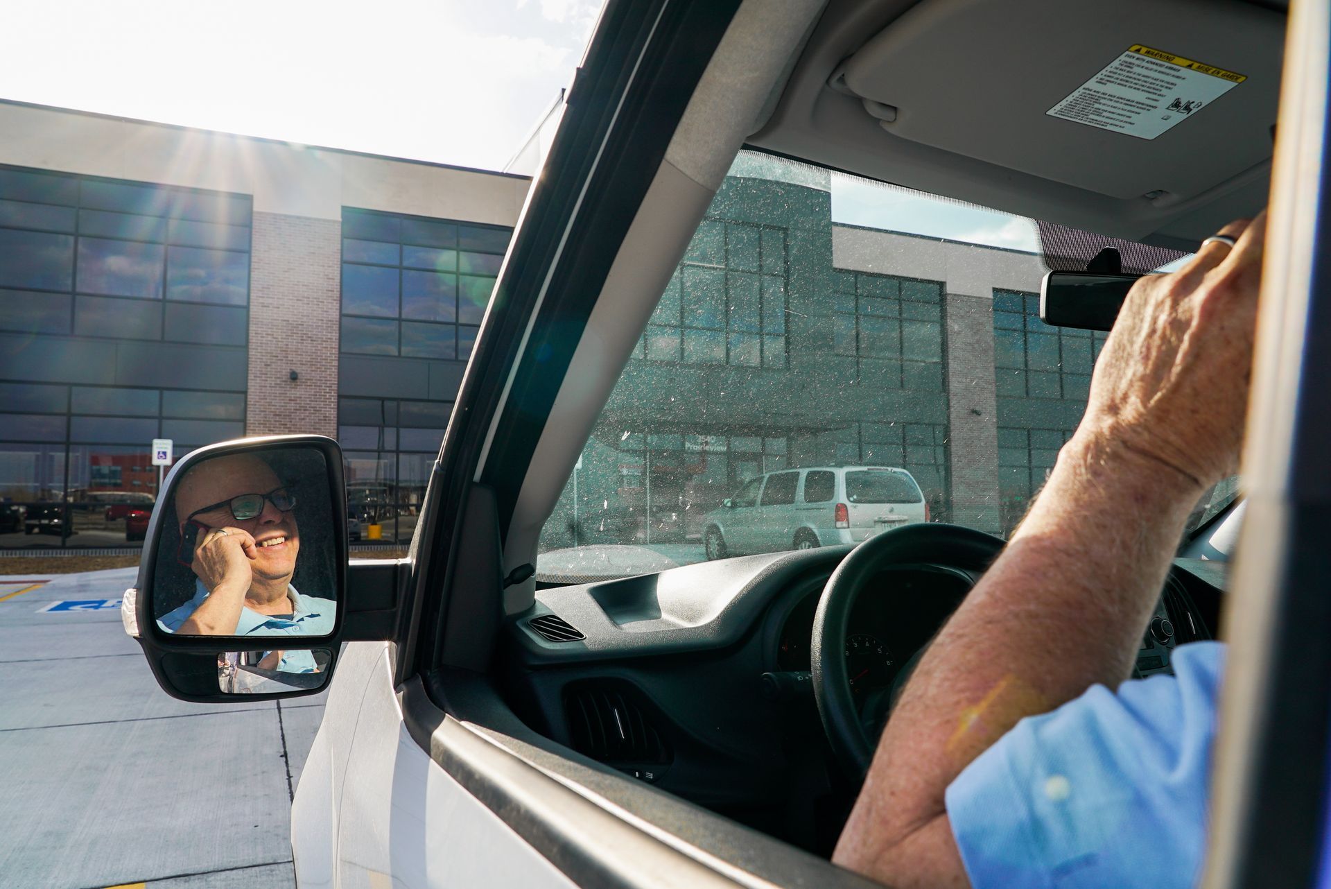 A man is driving a car and looking out the window at a building.