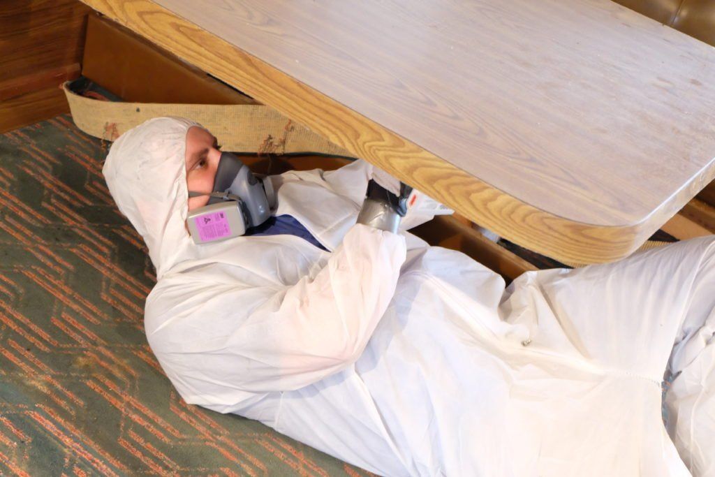 A man in a white suit is laying on the floor under a table.