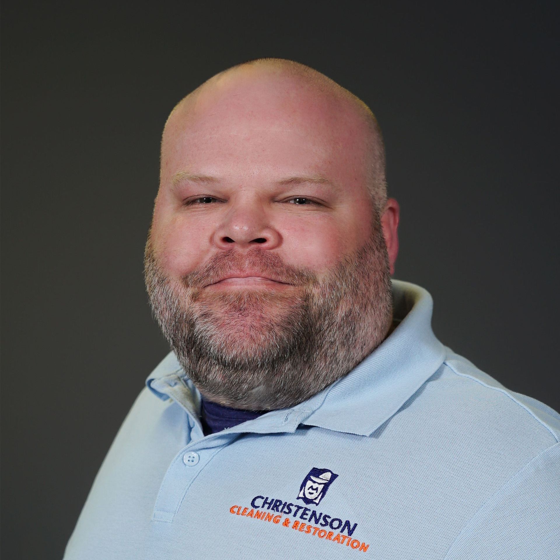 A bald man in a blue shirt is smiling for the camera.